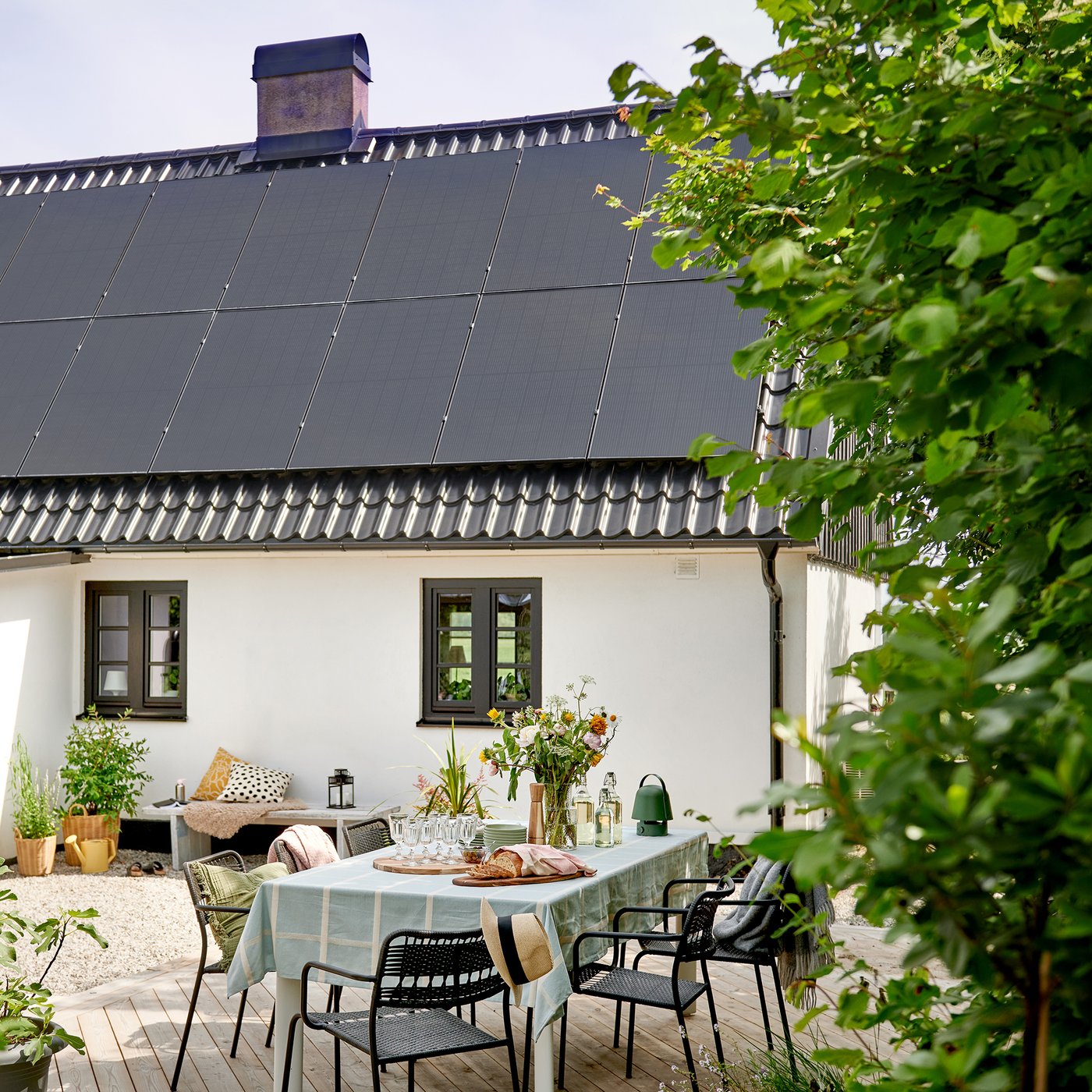 Ett hus med solpaneler och framför är en uteplats med utemöbler.