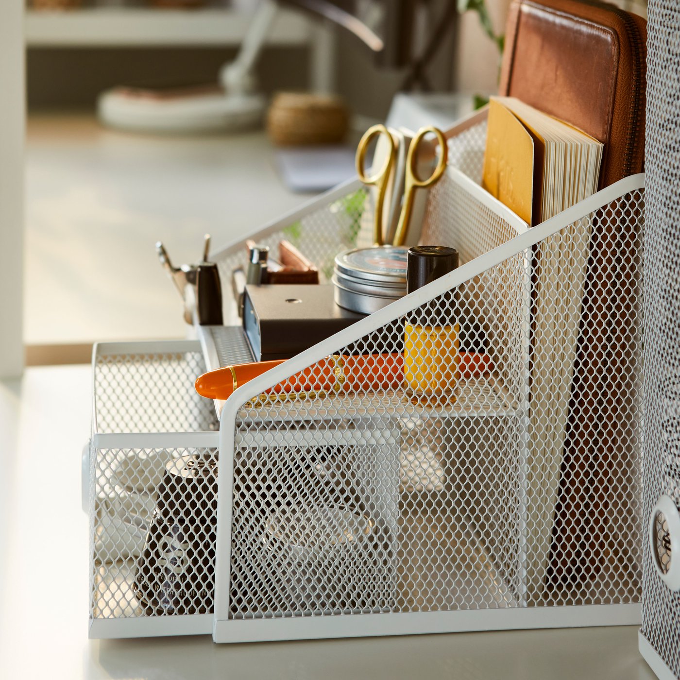 Ein Schreibtisch mit einem DRÖNJÖNS Schreibutensilienfach, in dem ein Stift, eine Schere und ein Notizbuch zu sehen sind