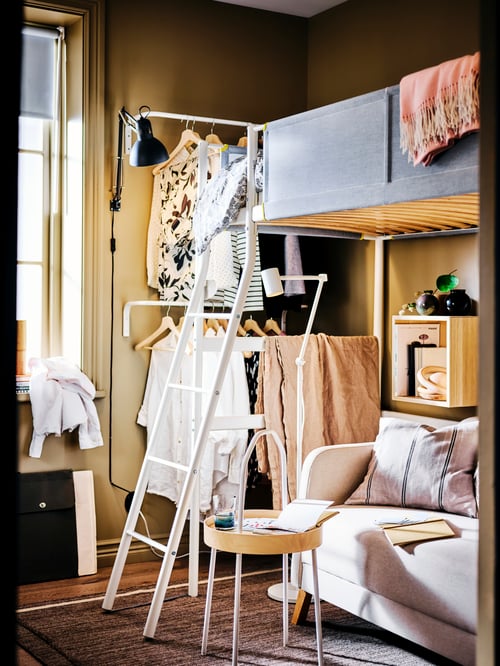Bedroom with a loft bed frame, a side table, and a work lamp. Under the bed frame is a sofa and a floor reading lamp.