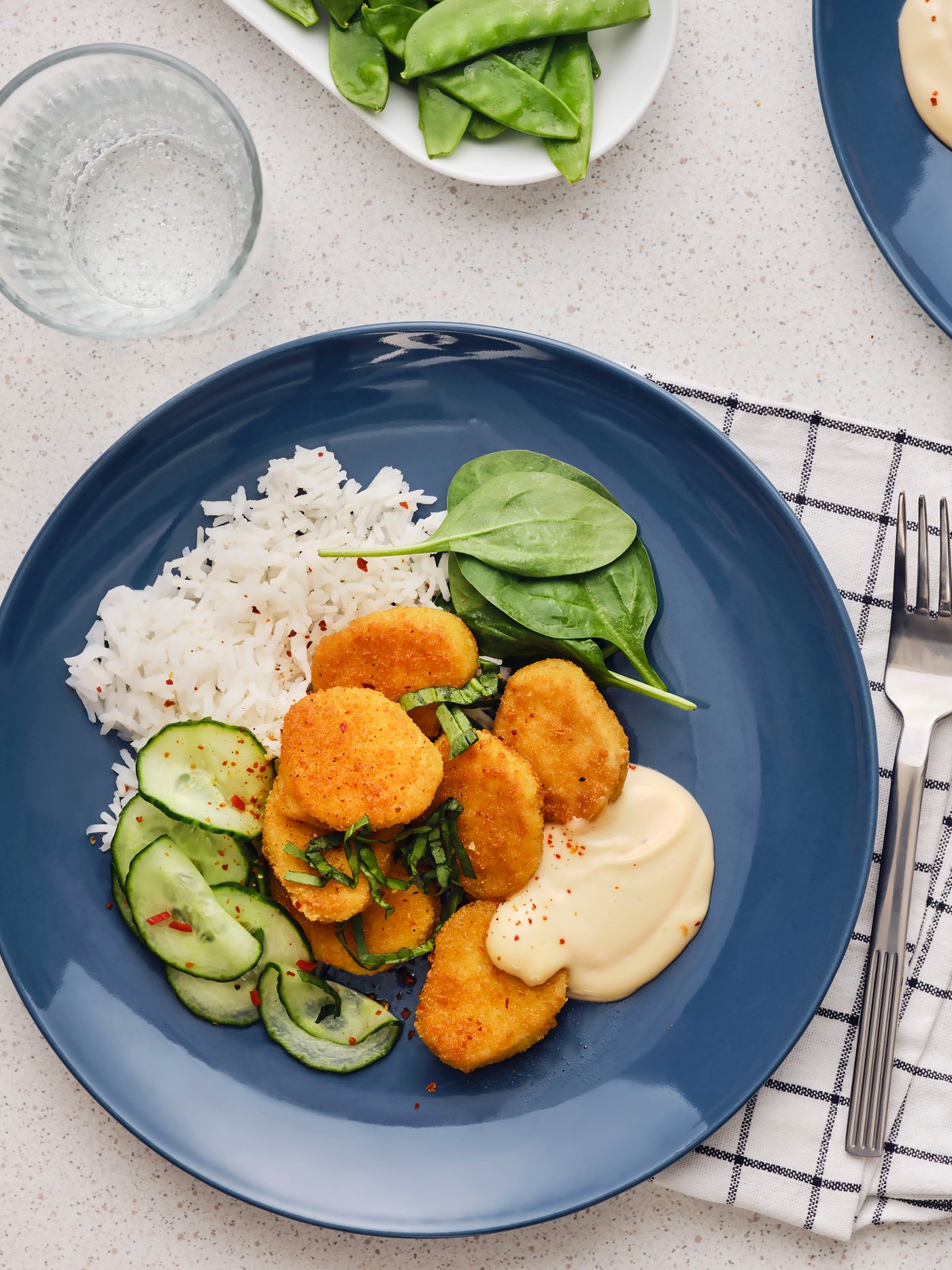 Sieben panierte Häppchen auf Weizenbasis werden auf einem blauen Teller mit Reis, Gurkensalat mit Chili und Sofamayonnaise serviert. 