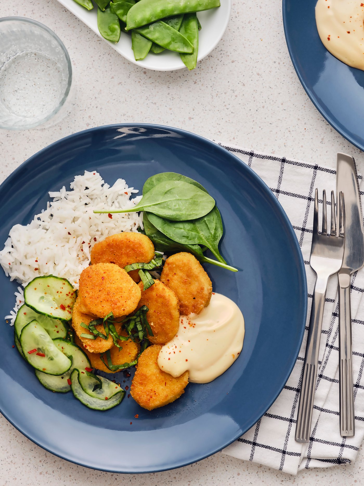 Sieben panierte Häppchen auf Weizenbasis werden auf einem blauen Teller mit Reis, Gurkensalat mit Chili und Sofamayonnaise serviert. 