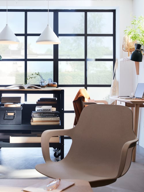 Un bureau à domicile moderne avec chaise pivotante à côté d’un bureau en bois et desserte avec livres, magazines et petite boîte de rangement.