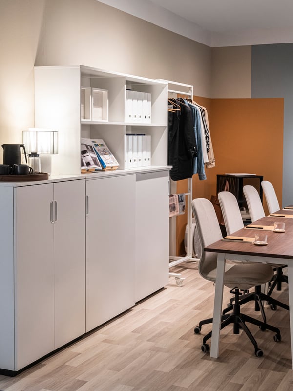 A white GALANT cabinet with doors sits in a meeting room in an office next to a table and chairs.