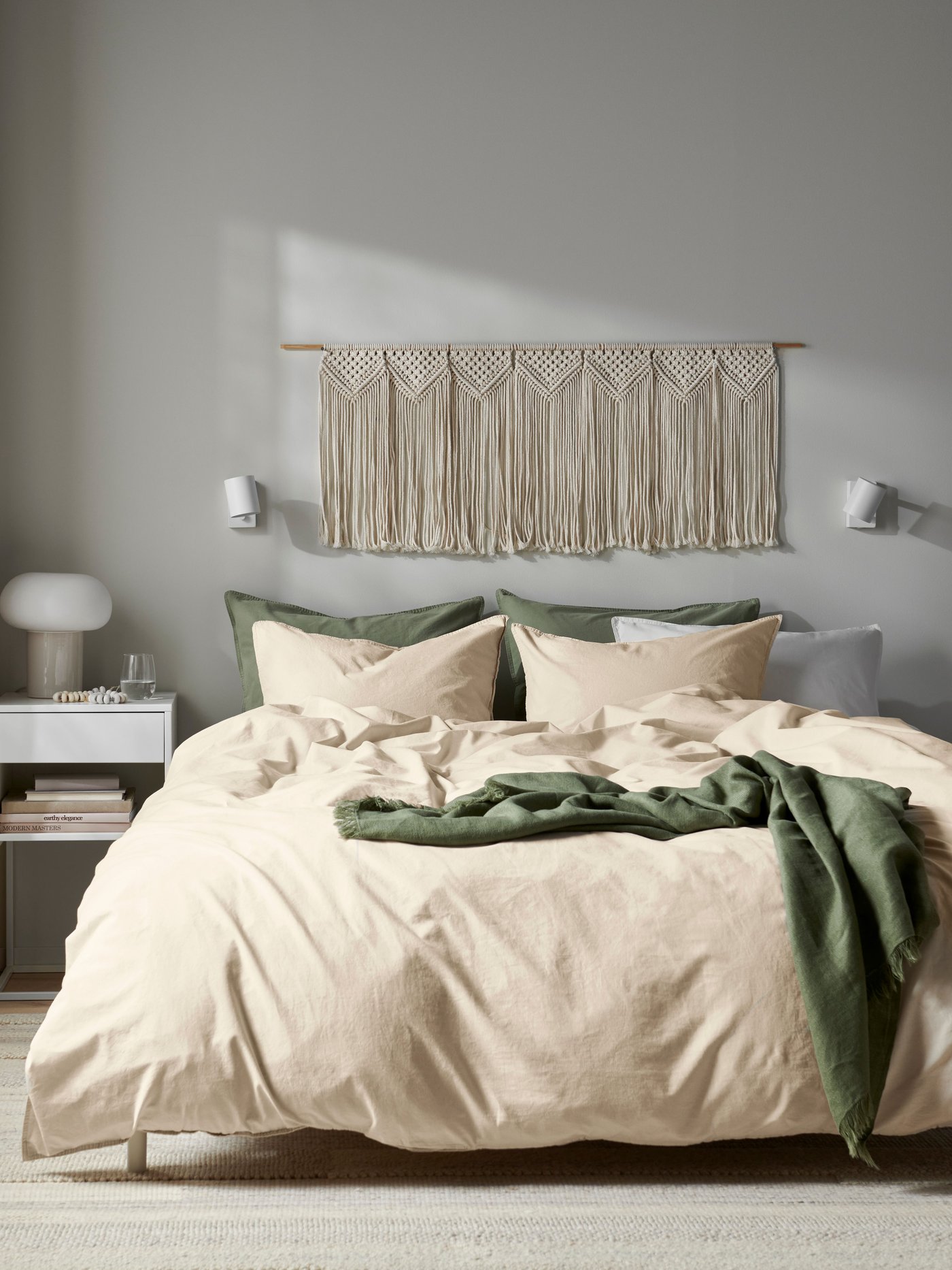 Una cama doble con plumón ÄNGSLILJA beige, una manta verde y almohadas.