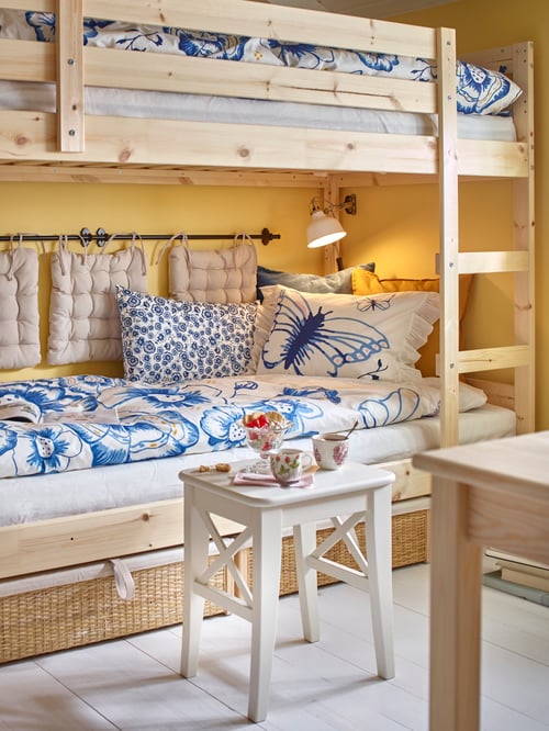 A pine MYDAL bunk bed frame with bedding displaying a butterfly design, a lamp, a wooden stool with cups and a wooden table.