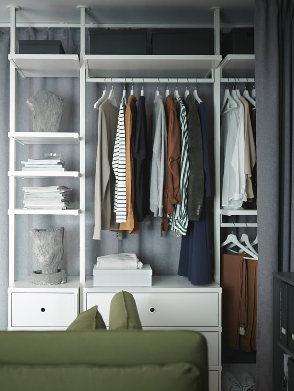 A white wardrobe with open and closed storage, integrated lighting, shirts on hangers, folded trousers, caps, white boxes.
