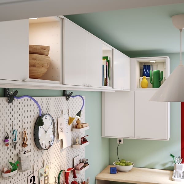A stylish kitchen featuring white VEDDINGE doors, complemented by decorative objects on shelves and a pegboard with hooks.