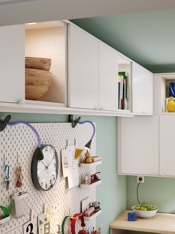 A stylish kitchen featuring white VEDDINGE doors, complemented by decorative objects on shelves and a pegboard with hooks.