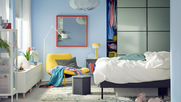 A SLATTUM upholstered bed stands in front of a SKYTTA/BOAXEL reach-in wardrobe with sliding doors near a SOTENÄS armchair.
