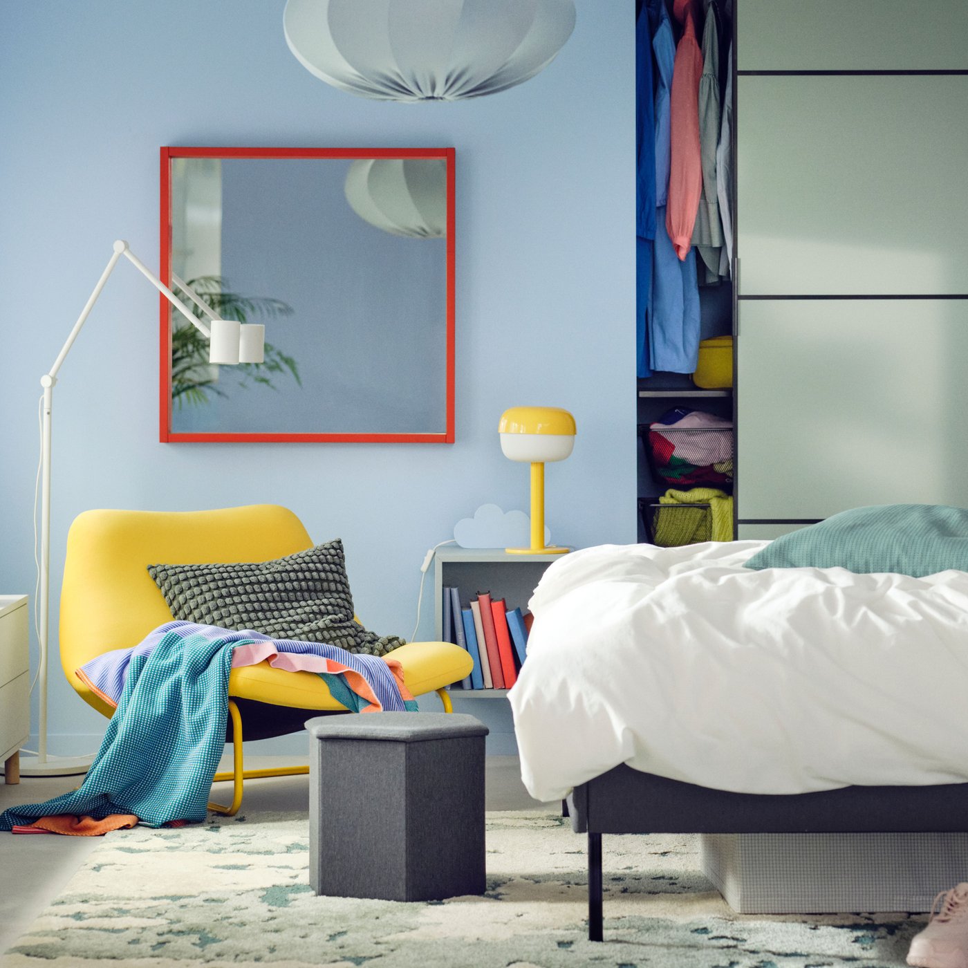 Letto imbottito SLATTUM vicino a una cabina armadio con ante scorrevoli SKYTTA/BOAXEL e a una poltrona SOTENÄS. Alla sinistra, un mobile basso e uno scaffale bianco su cui sono posizionate piante, lampade e contenitori trasparenti. 