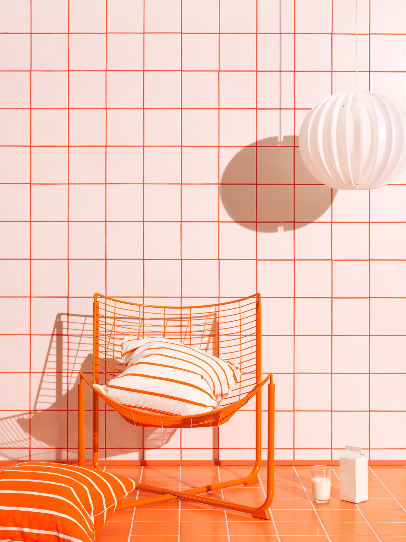 Prostor v beli in oranžni barvi z oranžnim vzglavnikom, oranžnim stolom in belo svetilko, ki visi s stropa.