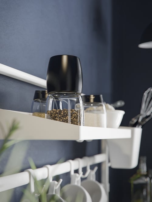 A modern kitchen featuring a small shelf mounted on a wall rail holding a black spice mill and several spice jars. 