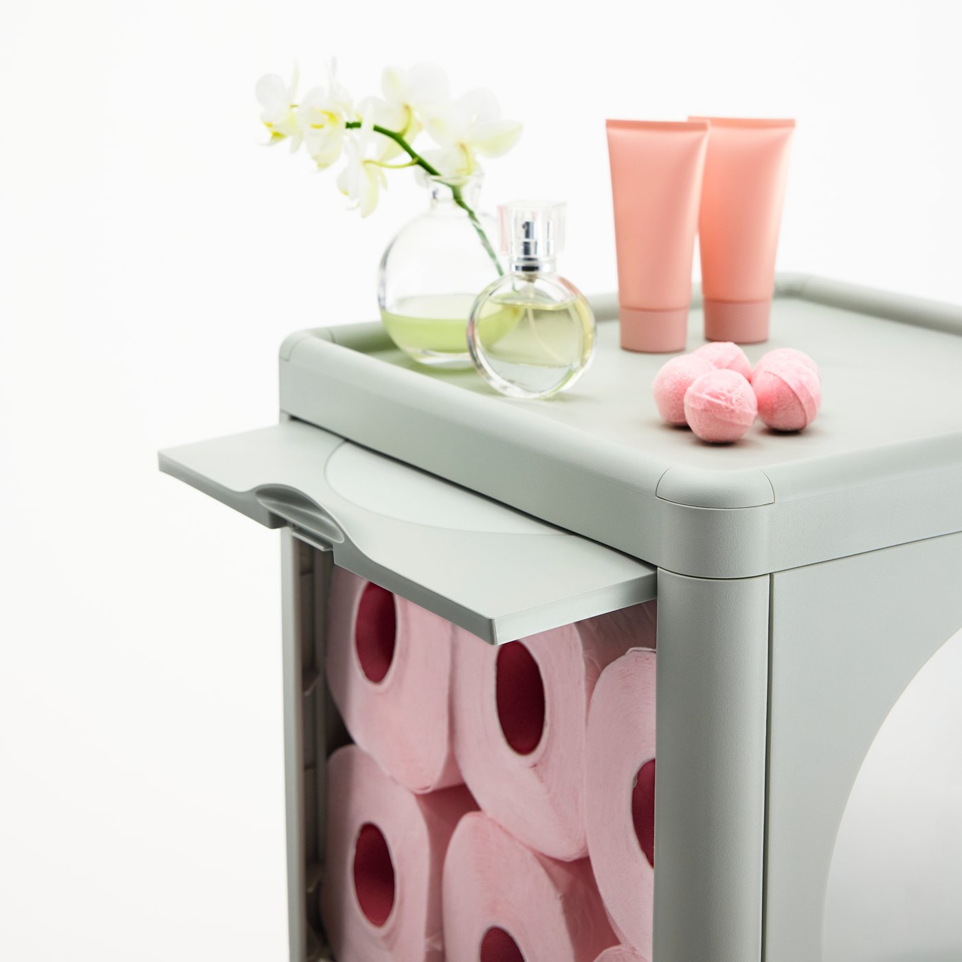 Nærbillede af et grønt IVÖSJÖN badeværelsesskab. Lyserøde toiletruller i et skab bag en låge med elegante lyserøde toiletartikler øverst.