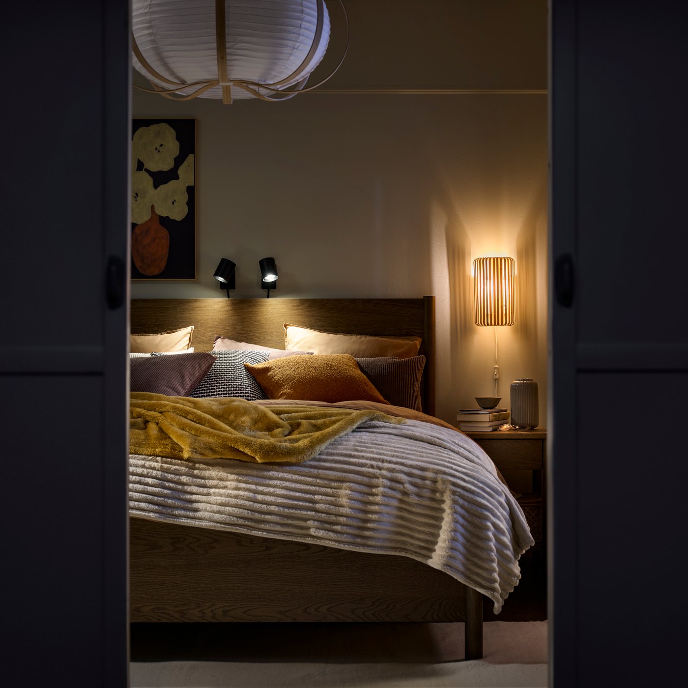Showing a scene through open doors of a bedroom with cosy lighting and a bed with throws and blankets.