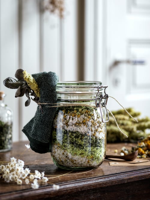A clear glass KORKEN jar with lid is filled with homemade potpourri; a dark green HIMLEÅN washcloth is tied at the rim.