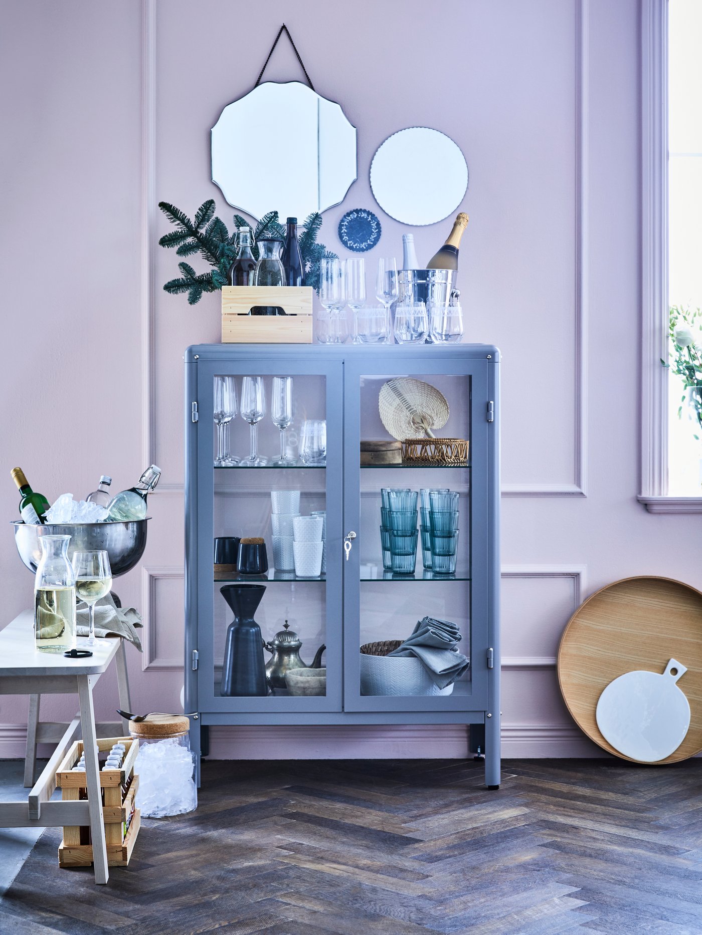 Una color gris con puertas de vidrio que permien ver los vasos y vajillas en el interior. Sobre la repisa hay unos espejos decorativos colgados en la pared.