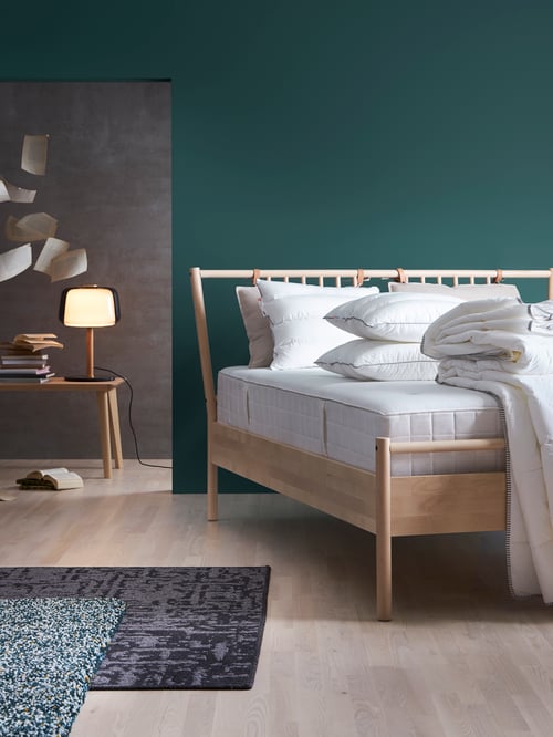 Bedroom with bed frame, pillow, table lamp, coffee table, pocket sprung mattress, folded quilt, two rugs, books, agendas.