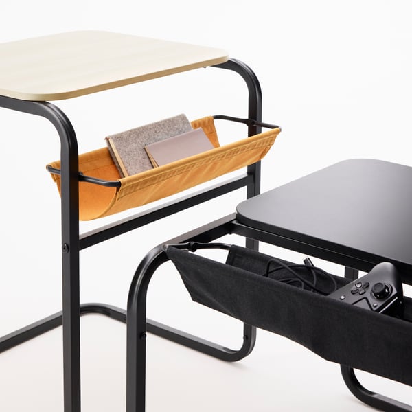Close-up of the adjustable canvas pouches of two OLSERÖD side tables. One contains game consoles, the other notebooks.