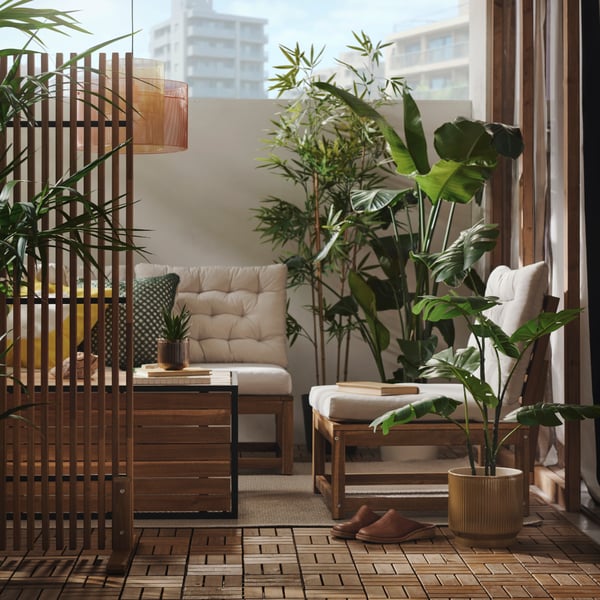 A balcony with light brown stained HÅKANSKÄR coffee table surrounded by plants and outdoor seating, creating a relaxing space.