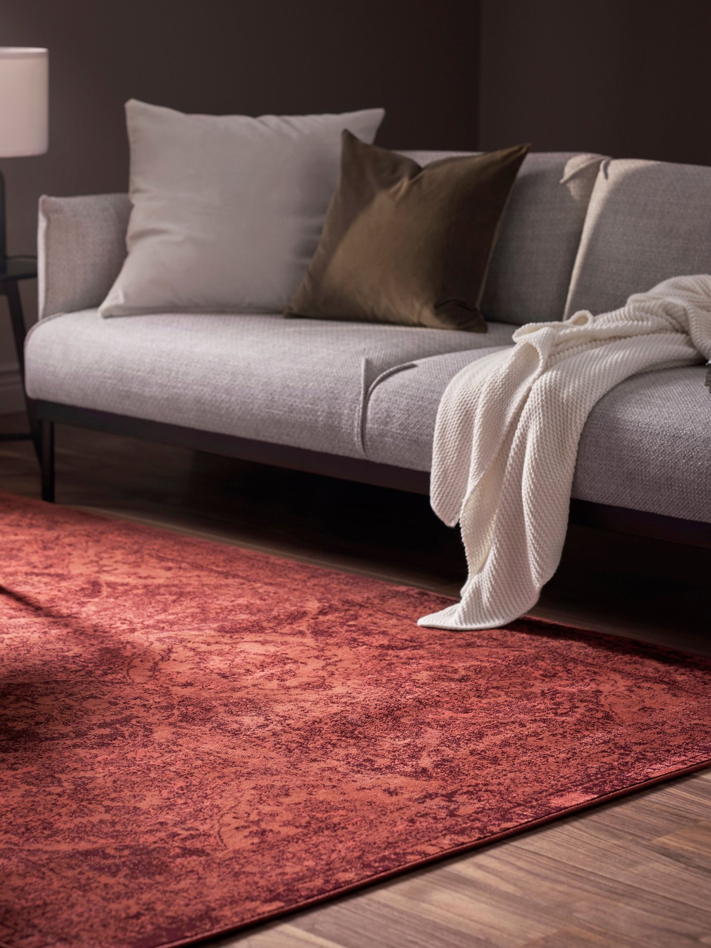 Tapis à poils ras rouge sous un canapé gris dans un salon. 