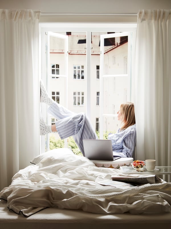 Eine Frau sitzt in einem geöffneten Fenster, links und rechts davon hängt die TERESIA Gardine.