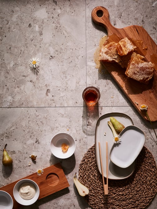 An artistic table collage with a wooden chopping board, beige dinnerware in rounded shapes and other natural objects.