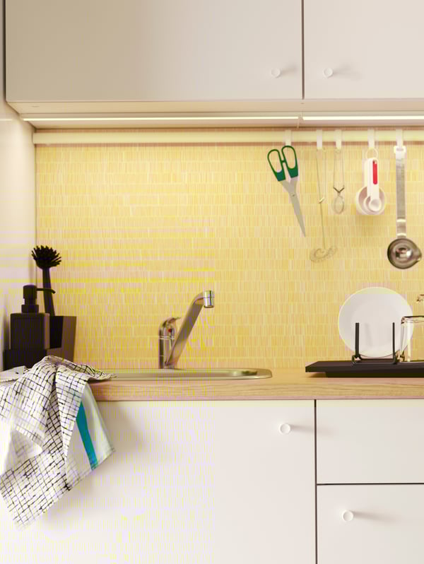 Kitchen with white doors, a yellow backsplash panel and rail with hooks where scissors and other kitchen utensils hang.