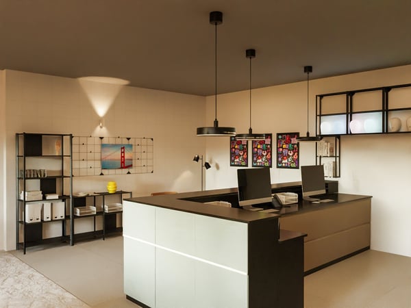 Teil einer Rezeption eines Hotels. Blick auf den Tresen mit Beleuchtung und zwei Monitoren. Dahinter offene Aufbewahrung und an den Wänden Bilder.