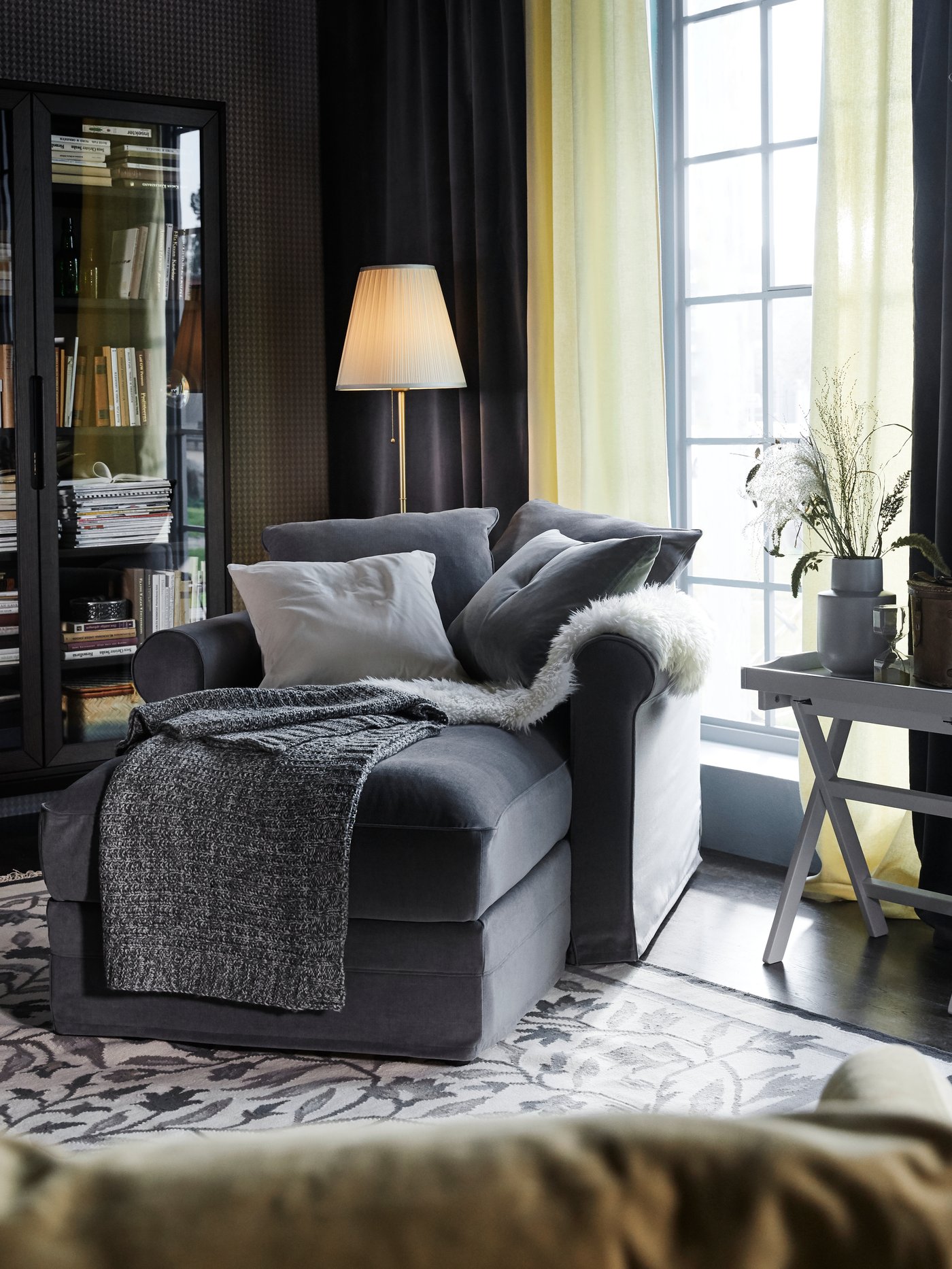 A living room with a grey single-seat GRÖNLID sofa, a grey throw blanket, and a rug on the floor.