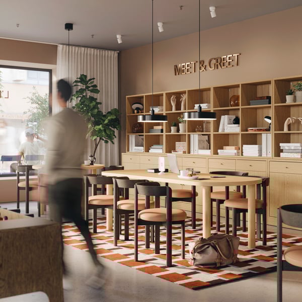 Meet-and-greet area in a hotel lobby with TONSTAD oak storage combinations, tables, chairs, and a man walking past the space.