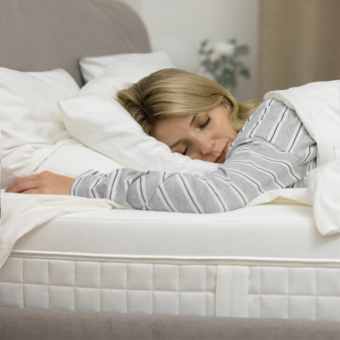 Spící žena v pruhovaném pyžamu na posteli, přikrytá bílou přikrývkou