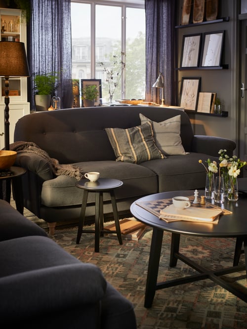 Living room area with a two-seat sofa with cushions, a round coffee table with vases, and a floor lamp.