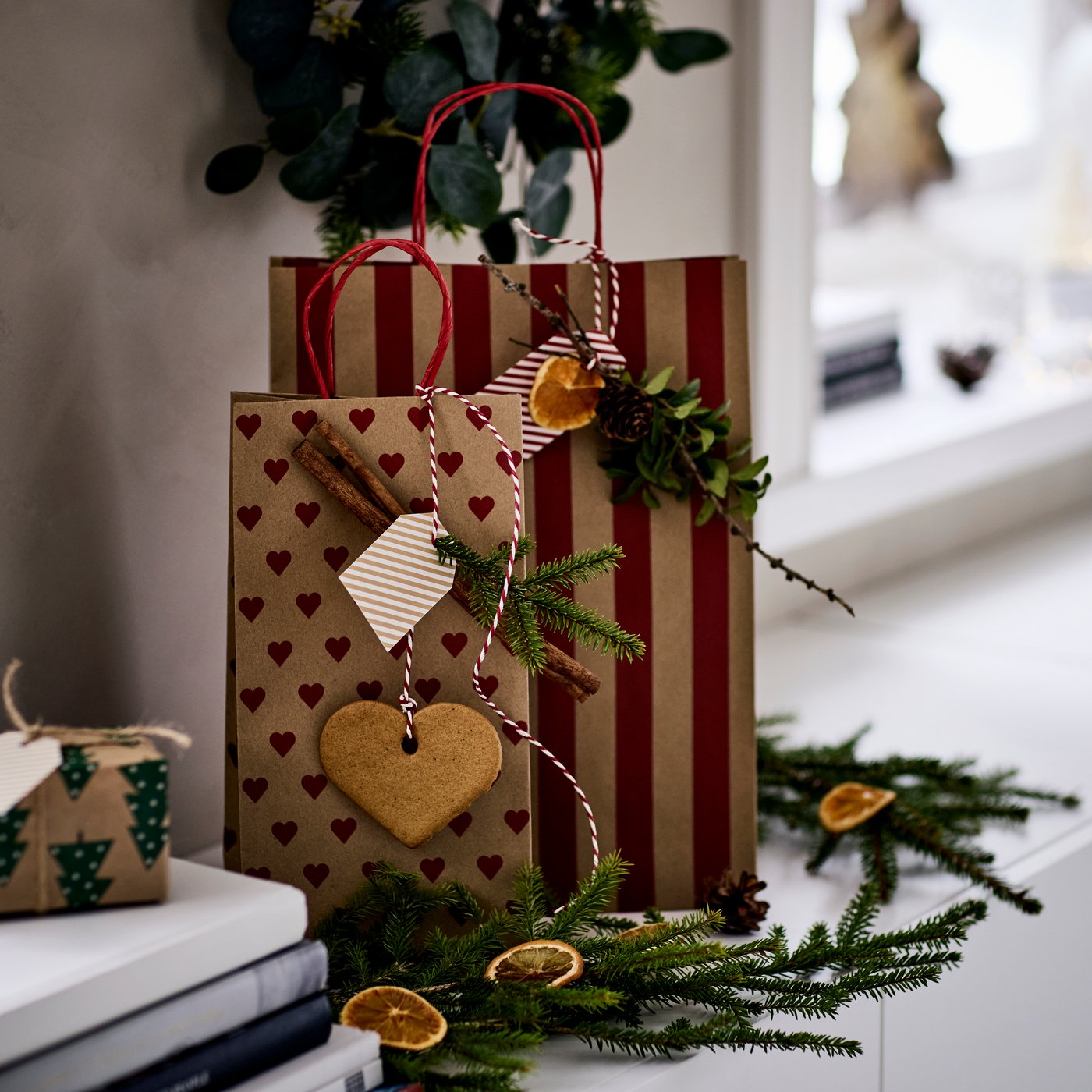 Two VINTERFINT gift bags, one with a heart pattern, the other with stripes, stand in a wooden box next to a small vase.