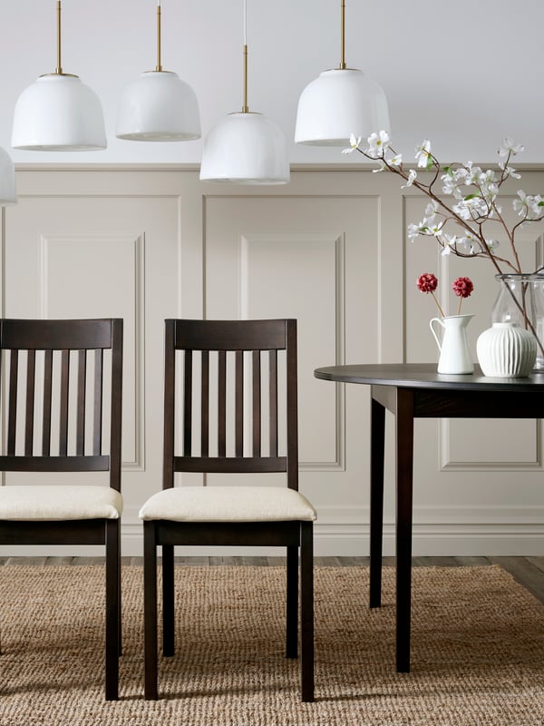 Four dark brown NÄSINGE chairs with light beige cushions are arranged around a black table in a stylish dining area.