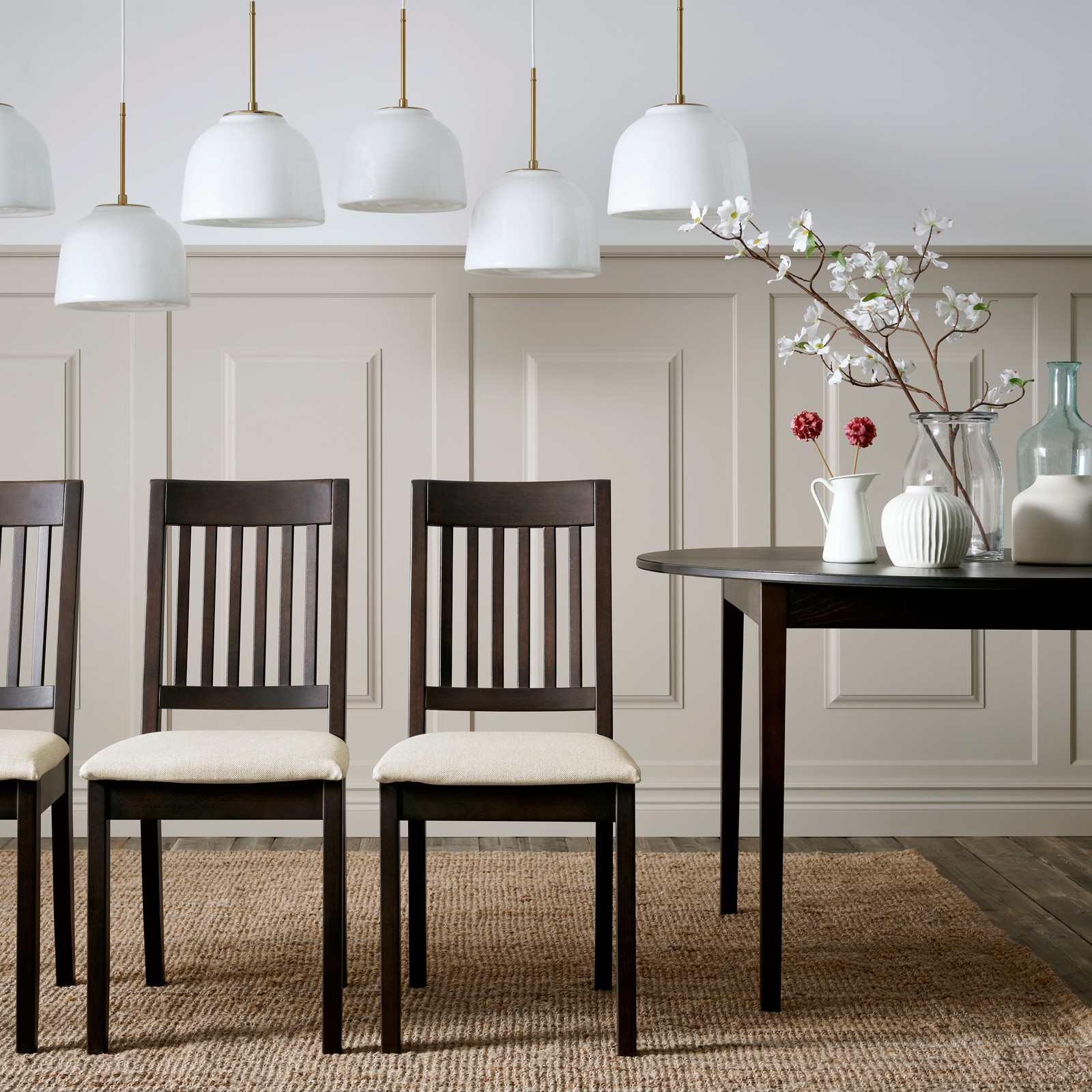 Four dark brown NÄSINGE chairs with light beige cushions are arranged around a black table in a stylish dining area.