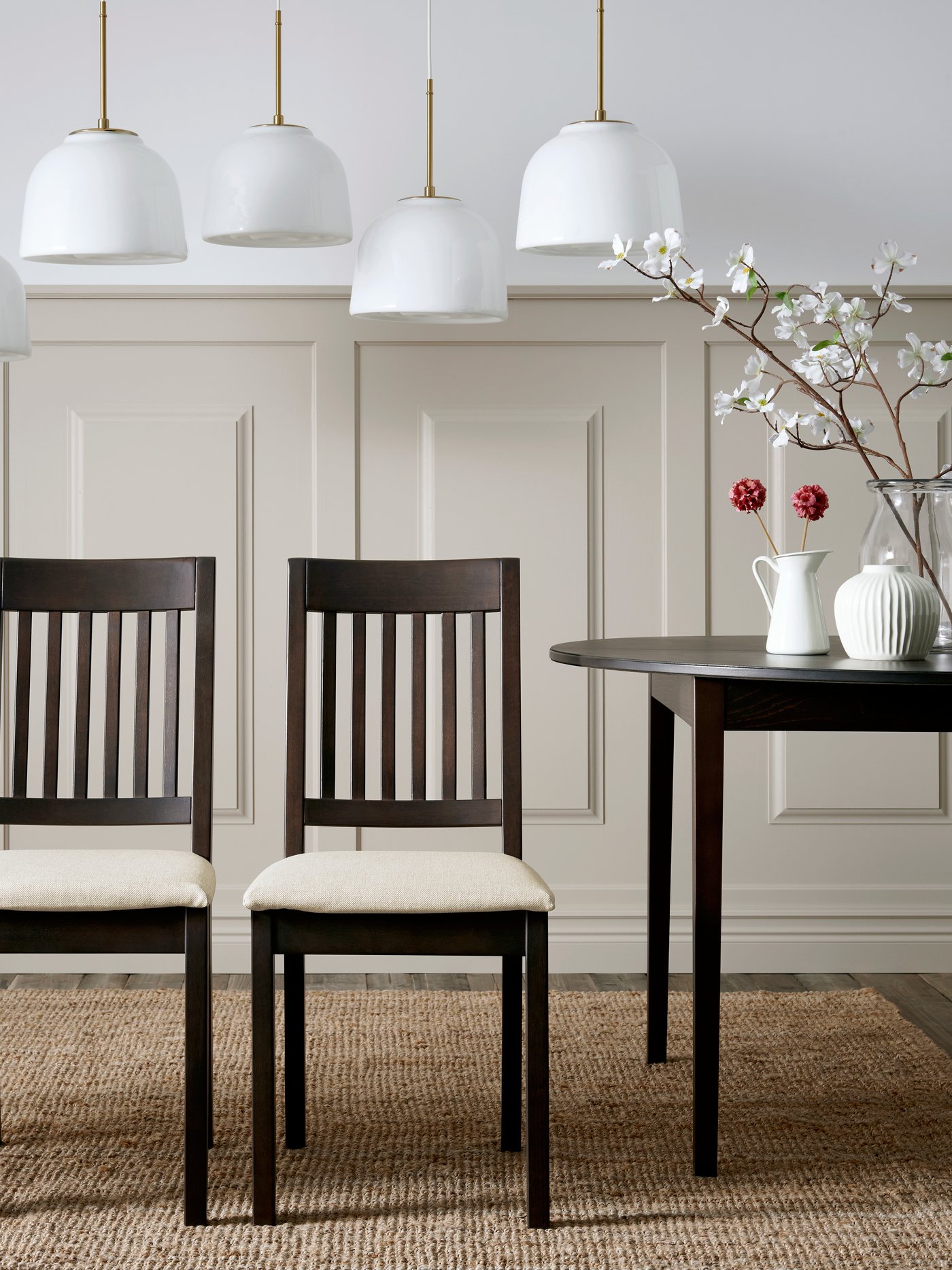 Quatre cadires NÄSINGE en marró fosc amb coixins beix clar al voltant d’una taula negra en una elegant zona de menjador.