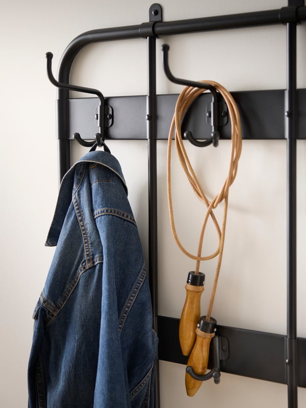 Close up of hooks on a black coat rack against a white hallway wall.