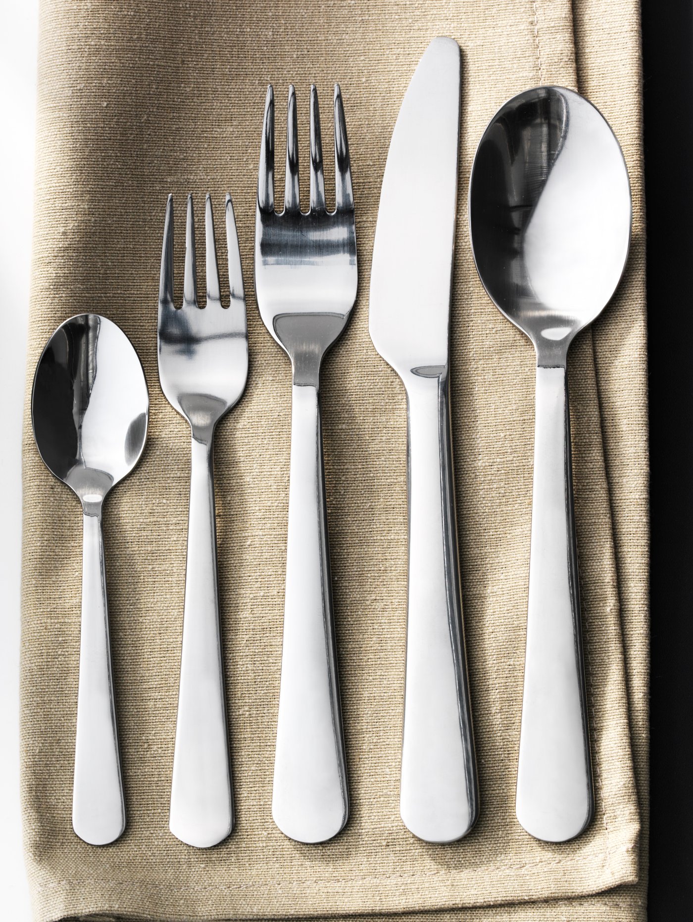 A DRAGON teaspoon, dessert fork, table fork, knife and table spoon laid out on a beige linen napkin.