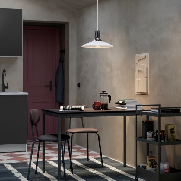 A modern kitchen area features a grey cabinet, minimalist black dining table, and a stylish pendant light hanging above.