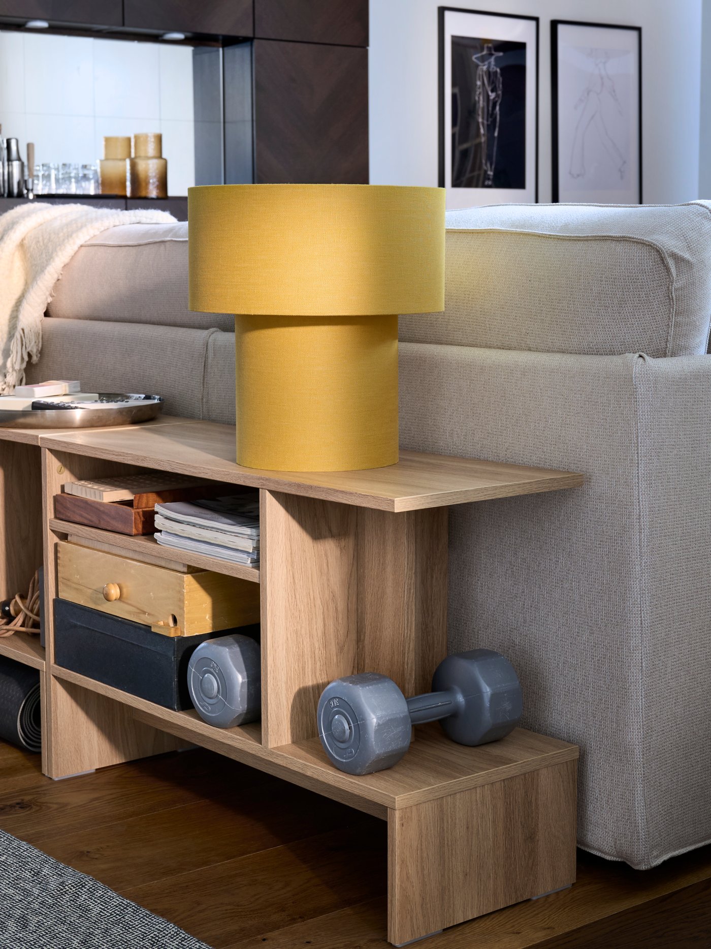 HOLMERUD sidetables with mixed contents and a yellow STOCKHOLM table lamp atop are placed along the back of a KIVIK sofa.