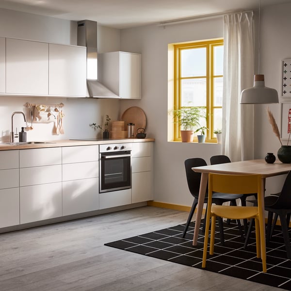 Man sieht eine minimalistische Küche mit matten, grifflosen Fronten und einer Arbeitsplatte aus Holz. Vor der Küche steht auch ein LISABO Esstisch mit vier Esszimmerstühlen.