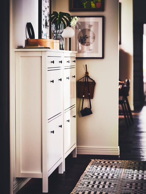 Close-up on hallway with two rectangular white wooden shoe cabinets with 2 compartments holding decorations.