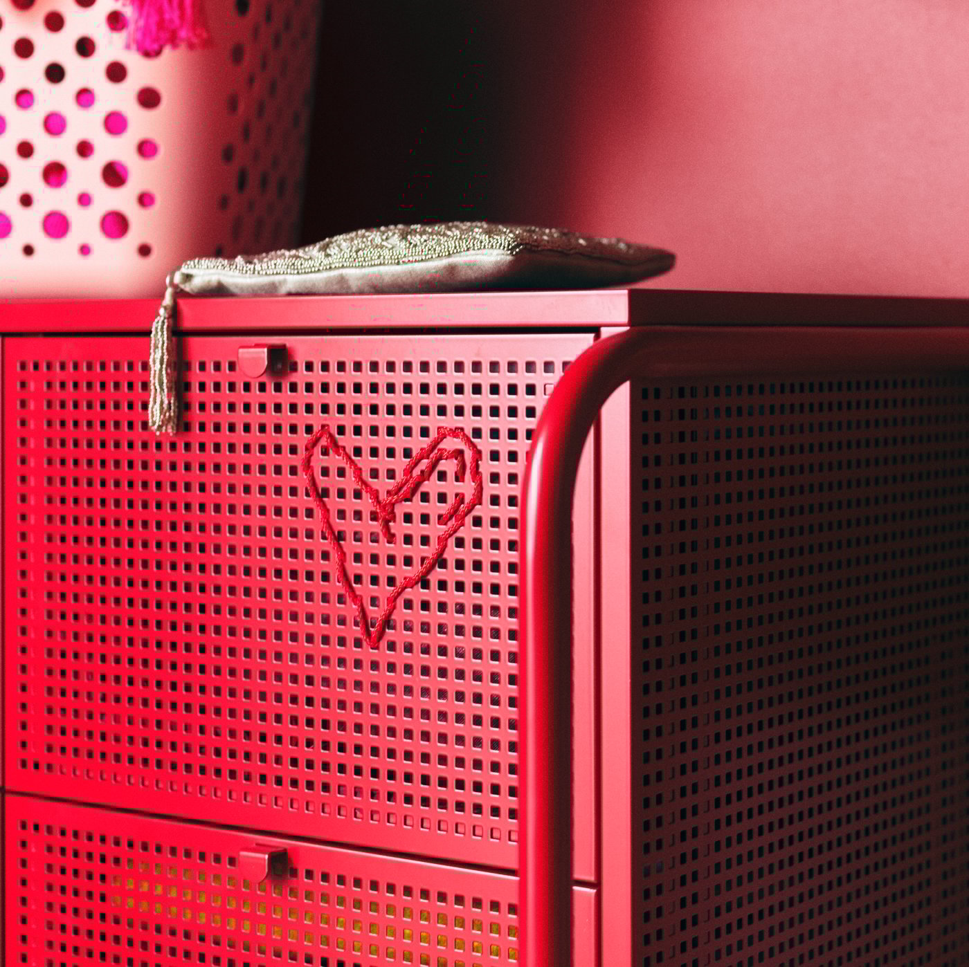 A red NIKKEBY chest of drawers with a red heart embroidered on it and a zip-lock purse on top.