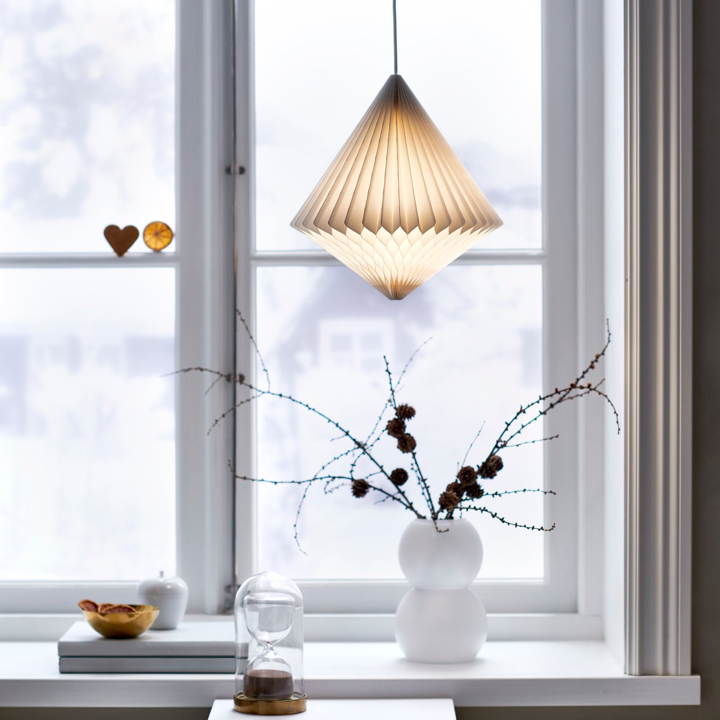 En hvit lampeskjerm av papir henger foran vinduene.