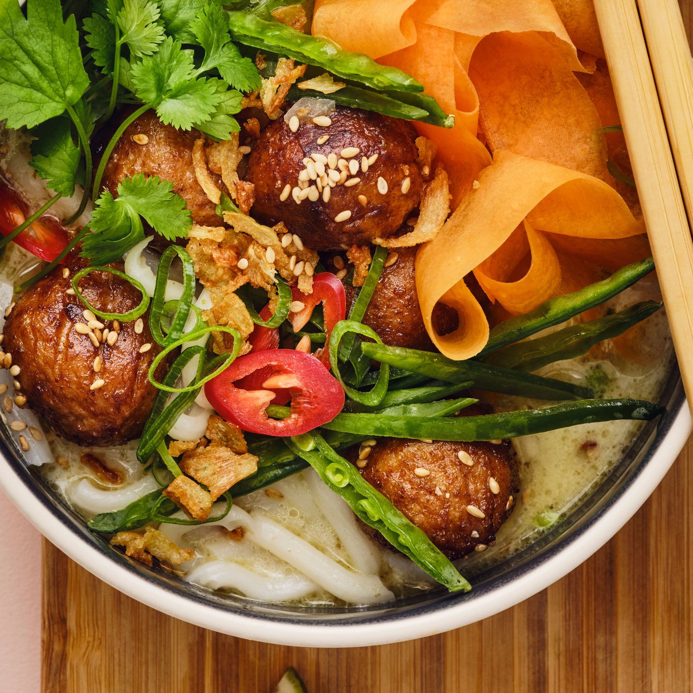 Tre ciotole contenenti pietanze dai sapori asiatici su una superficie in bambù. Su una delle ciotole sono appoggiate delle bacchette.