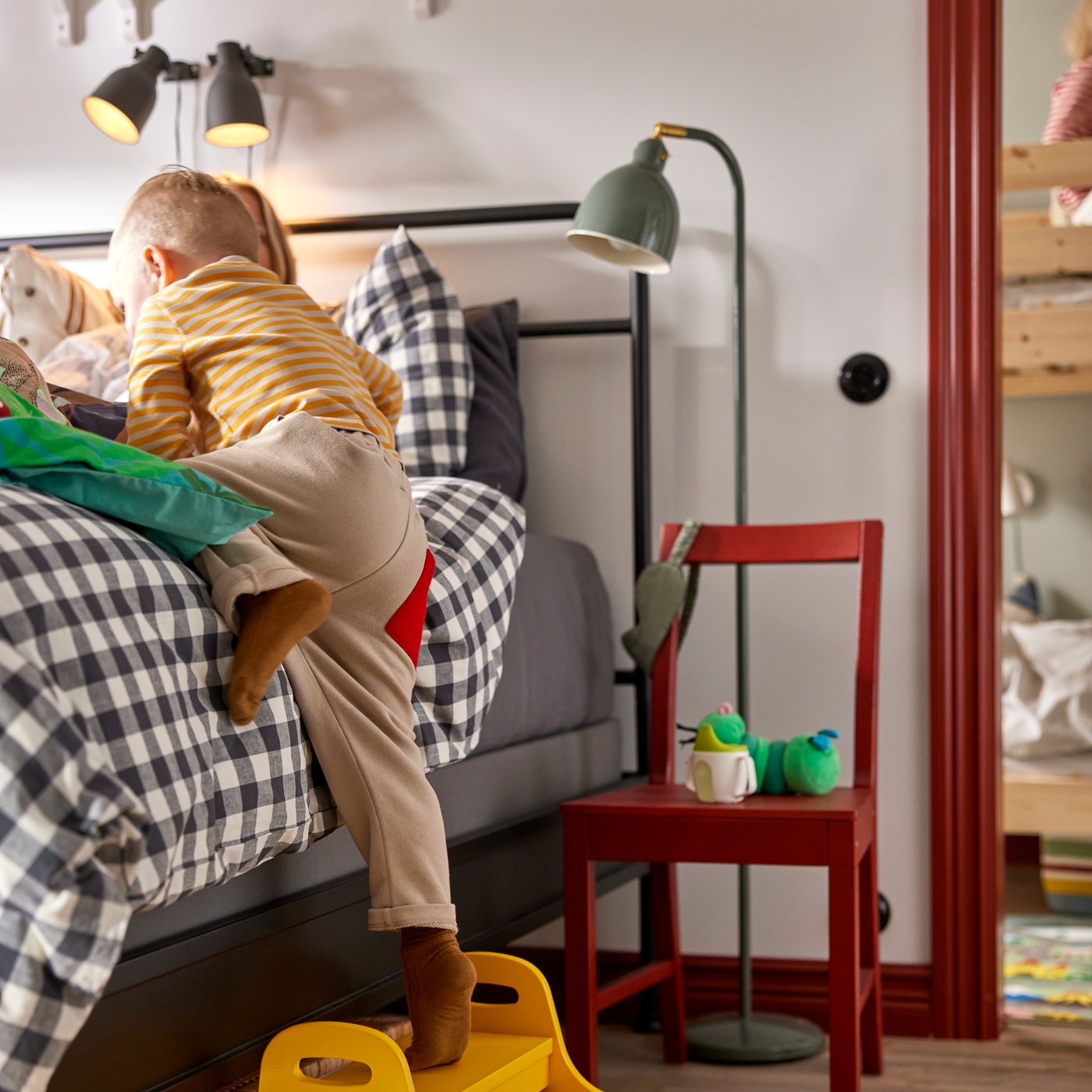 Small child climbing up to parents’ bed on yellow TROGEN children’s step stool. Red wooden chair used as bedside table.