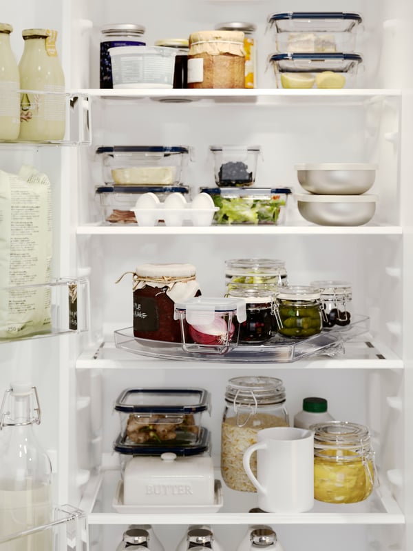 Réfrigérateur ouvert, révélant quatre tablettes où sont placés des récipients remplis d’aliments. Sur une des tablettes, plateau pivotant SNURRAD accueillant des bocaux.
