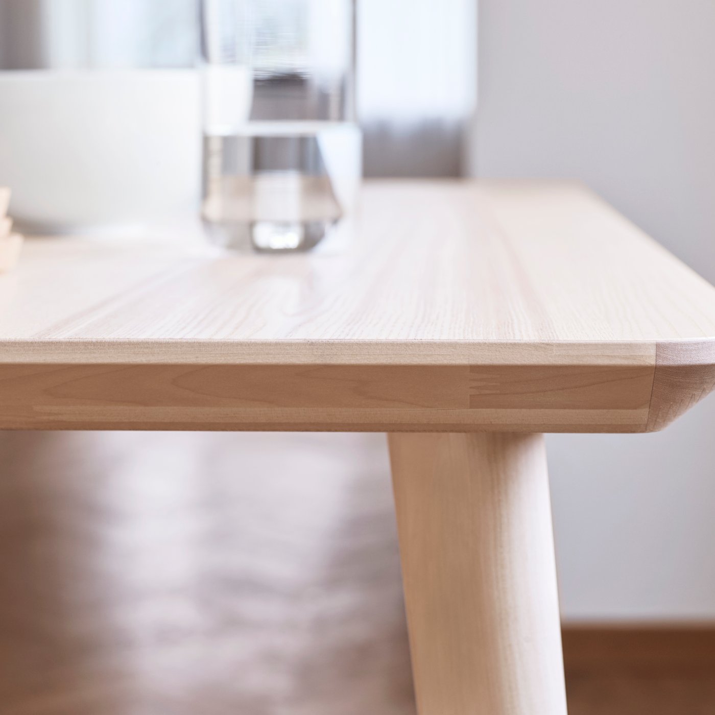 The smooth edge of a light-coloured LISABO coffee table highlighting the ash veneer material, with a glass of water on top.