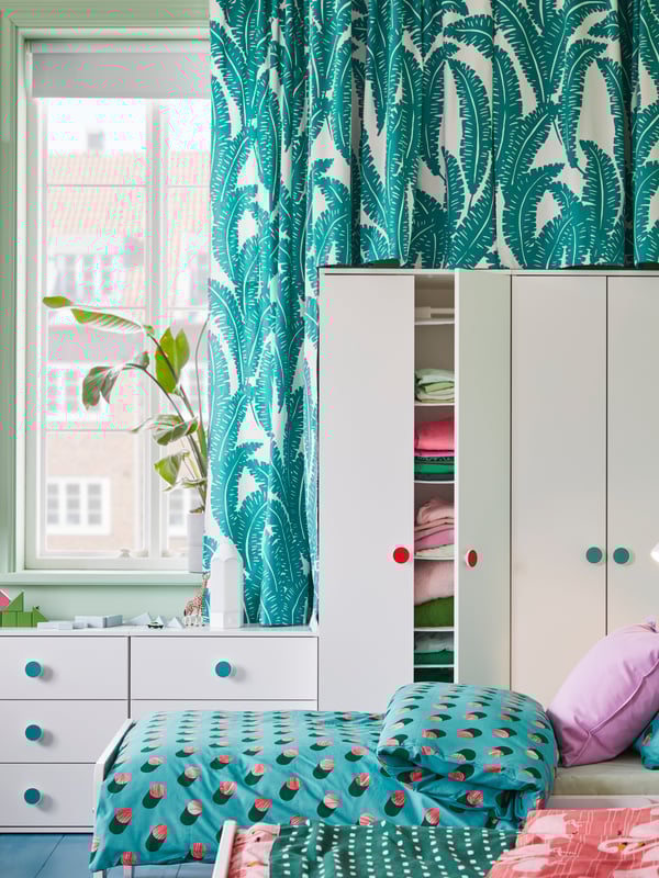 A SLÄKT bed with GRACIÖS bed linen stands in front of GODISHUS wardrobes and a window in a children’s bedroom.