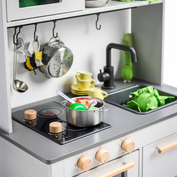 Close-up of a SILLTRUT play kitchen. There’s a pot on the stove and some greens in the sink.